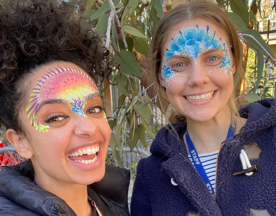 Two young smiling women with their faces painted in a delicate design