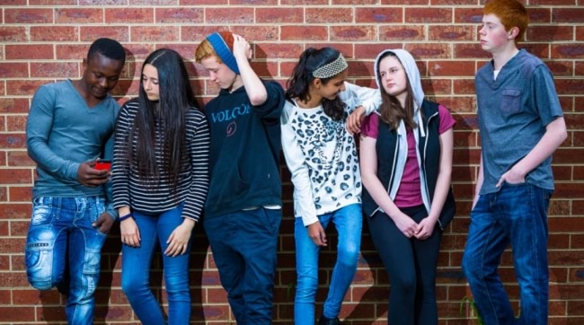 Six teenagers leaning against a brick wall. 