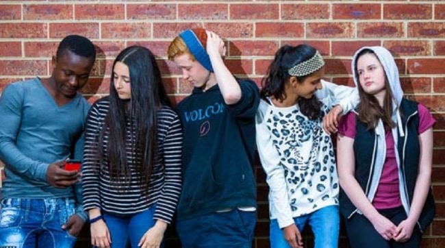 Group of young people standing against a brick wall.